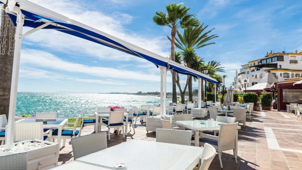 A scenic view of some of the best restaurants in Marbella, showcasing elegant outdoor dining areas, with tables set up on sunny terraces overlooking the Mediterranean coast. The ambiance reflects fine dining with a mix of traditional Spanish and contemporary cuisines, offering a luxurious and inviting atmosphere.